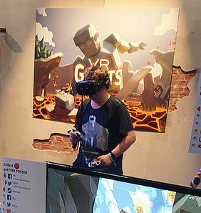 Wieland hat eine VR-Brille auf und steht vor einem großen Plakat