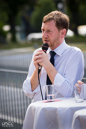 Der Sächsische Ministerpräsident Michael Kretschmer steht in einem weißen Hemd an einem Cocktailtisch und spricht in ein Handmikrofon. (Archivbild)